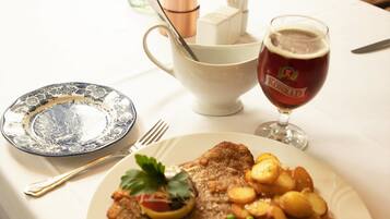 Une table à manger avec une assiette de nourriture, un verre de bière et un vase rempli de fleurs.