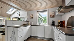 Een moderne keuken met witte kastjes, een houten aanrecht, een dakraam en een raam met uitzicht op groen.