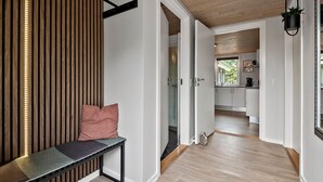 Een modern interieur met een bank, een wand van houten latten en een zichtbare keuken door een open deur.