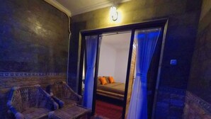 A room with a wicker chair, a small table, and a bed with orange pillows. - Tropical Garden Inn (Penida Island)