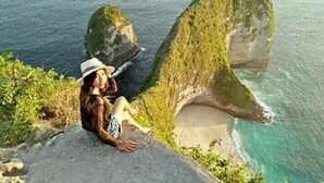 A person sitting on a rock by the sea with a large rock formation nearby. - Tropical Garden Inn (Penida Island)