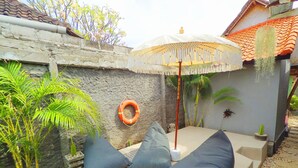 A poolside area with a seating arrangement, a life ring, and a decorative umbrella. - Tropical Garden Inn (Penida Island)