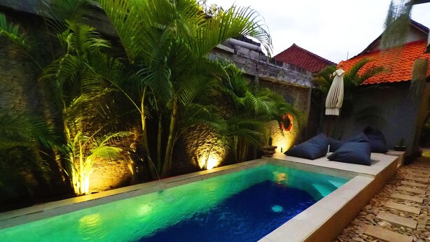 A rectangular swimming pool with a tiled edge, surrounded by a stone wall and lush greenery. - Tropical Garden Inn (Penida Island)