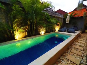 A rectangular swimming pool with a tiled edge, surrounded by a stone wall and lush greenery. - Tropical Garden Inn (Penida Island)