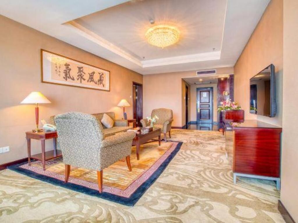 Une chambre d’hôtel avec un canapé, des fauteuils, une télévision, un bureau et une moquette à motifs.
