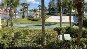A tennis court surrounded by palm trees and a building with a beach view. - Sunset beach getaway (Treasure Island)