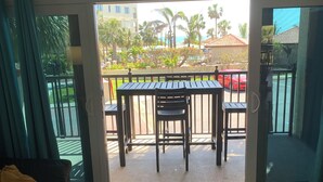 A living room with a sofa, a coffee table with remotes, and a sliding glass door leading to an outdoor patio with a table and chairs. - Sunset beach getaway (Treasure Island)