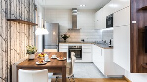 A modern kitchen with white cabinets, stainless steel appliances, and a wooden dining table with chairs. - goodhome Browar Lubicz (Kraków)