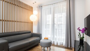 A modern living room with a grey sofa, a round ottoman with oranges, a wooden slatted wall, and a TV on a black stand. - goodhome Browar Lubicz (Kraków)
