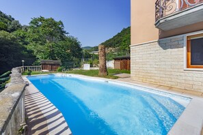 A swimming pool with a stone border, a wooden deck, and a view of a hillside.