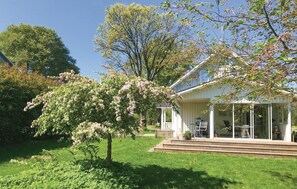 Una casa blanca con un porche cubierto y un jardín con árboles florecientes.