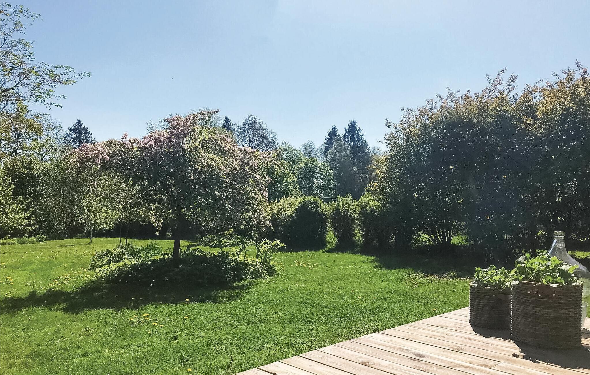 Un jardin bien entretenu, agrémenté d’une terrasse en bois, d’une pelouse verdoyante et de divers arbres.
