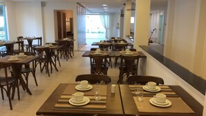A spacious dining area with multiple tables and chairs, arranged in a linear fashion with a view to the outside. - Scenarium Hotel (Jaboatão dos Guararapes)