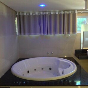 A modern bathroom with a freestanding bathtub, a vanity with a mirror, and a window with curtains. - Scenarium Hotel (Jaboatão dos Guararapes)