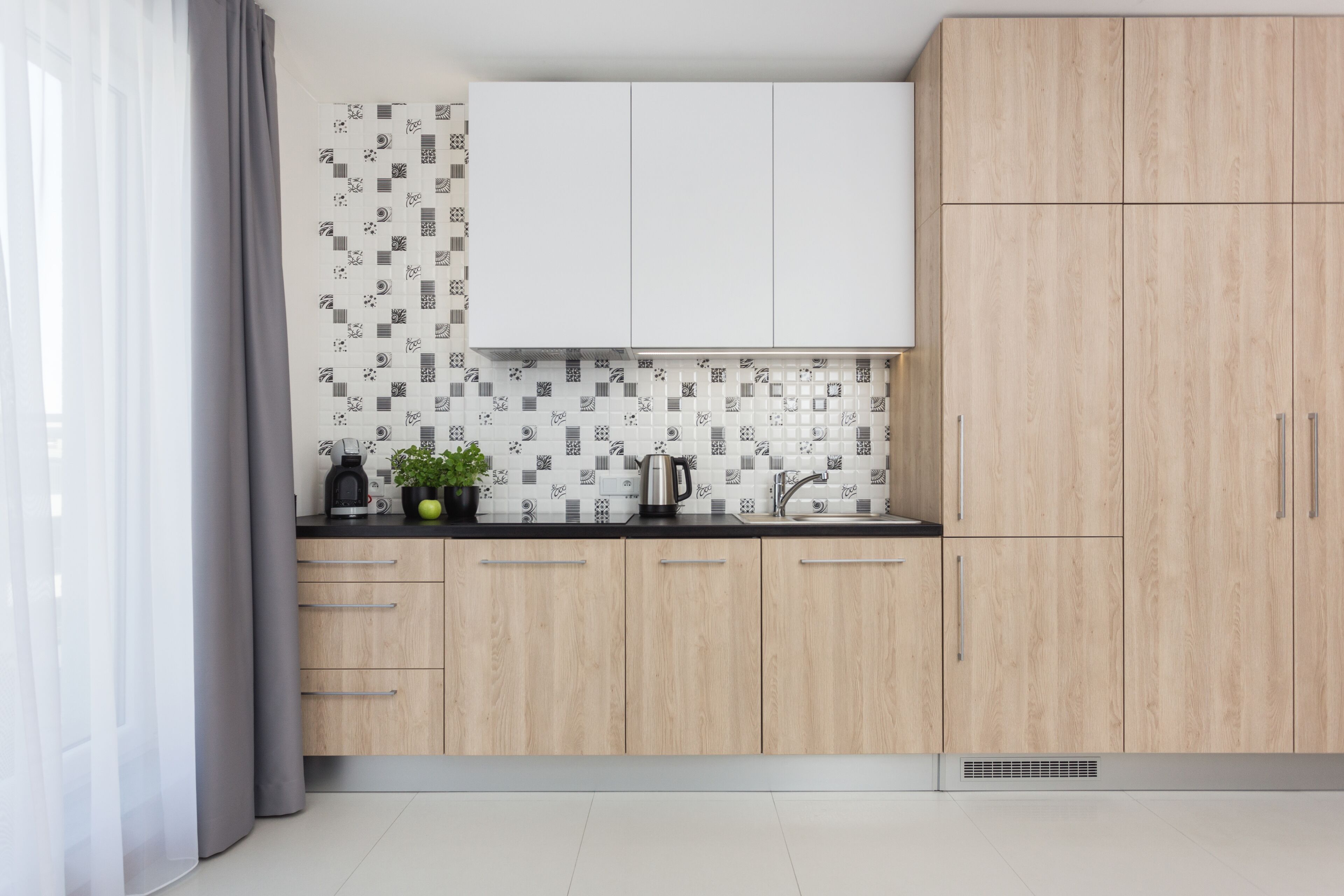 Uma cozinha moderna com armários de madeira clara, bancada preta e painel de fundo estampado.