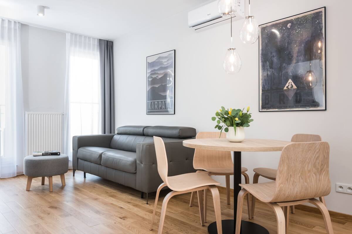 A modern living room with a grey sofa, a round wooden dining table, and a potted plant.