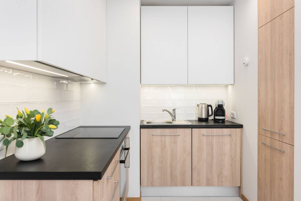 A modern kitchen with white cabinets, a black countertop, and a stainless steel coffee maker.