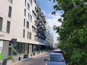 A modern building with multiple floors, large windows, and balconies. There are potted plants along the sidewalk and a no parking sign visible.