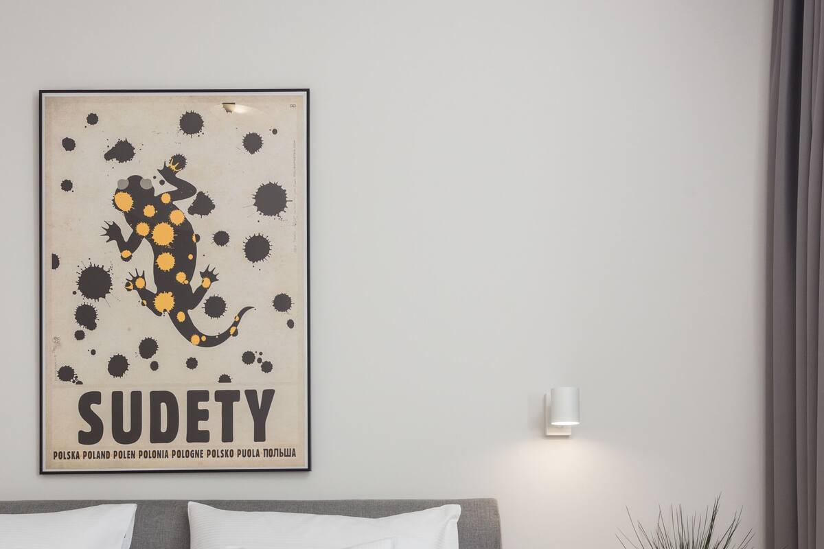A modern bedroom with a large bed, a bedside table with a lamp, a wall-mounted shelf, and a poster on the wall.