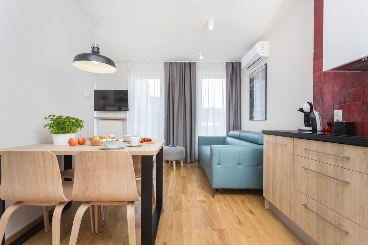 A modern kitchen with wooden cabinets, a dining area with two chairs, a blue sofa, and a potted plant.