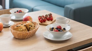 Uma sala de estar moderna com um sofá azul, uma mesa de madeira com itens de café da manhã e uma luminária pendente preta.