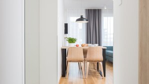 Cozinha moderna com área de jantar, destacando uma mesa e cadeiras de madeira, uma luminária pendente e vista para a sala de estar.