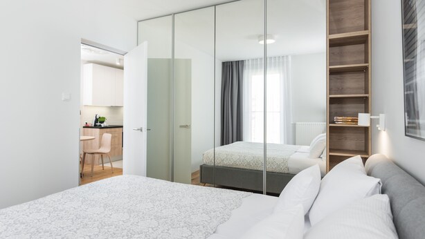 Um quarto moderno com um espelho grande, uma cama, uma mesinha de cabeceira e uma estante embutida.