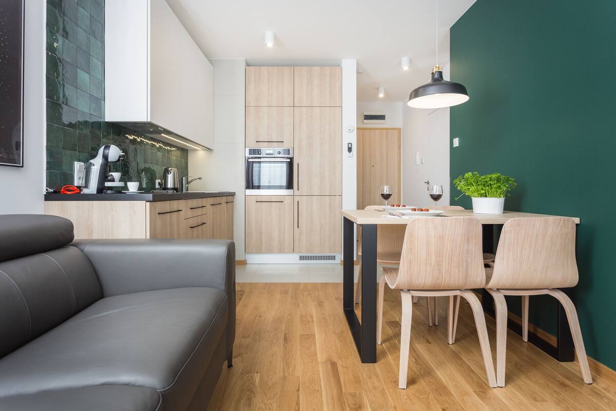 A modern kitchen with wooden cabinets, a built-in oven, and a dining area with a table and chairs.
