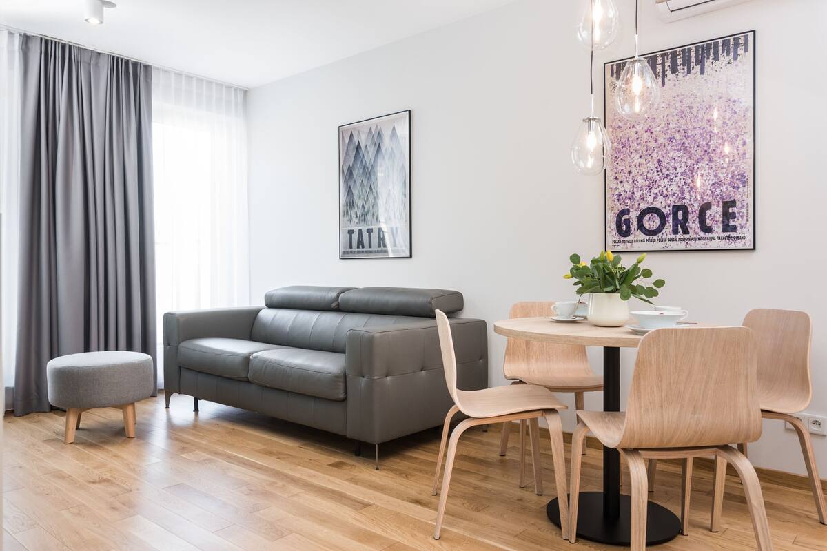 A modern living room with a grey sofa, wooden floor, and a dining area with a round table and chairs.