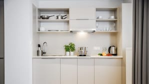 A modern kitchen with white cabinets, a stainless steel range hood, and a countertop with a kettle, a plant, and some fruits. - Micro Apartments Kazou Residence (Warsaw)