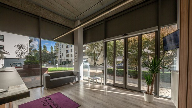 A modern reception area with a sofa, a small table, and a purple rug with text. - Micro Apartments Kazou Residence (Warsaw)