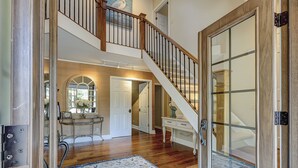 Un vestíbulo amplio con una escalera de madera, una puerta de cristal y un espejo decorativo.