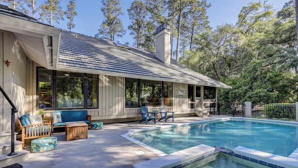 Un área de piscina con jacuzzi, mobiliario exterior y un porche cubierto.