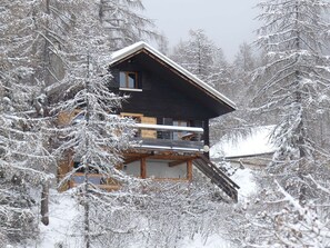 A cabin with a wooden deck, surrounded by snow-covered trees.