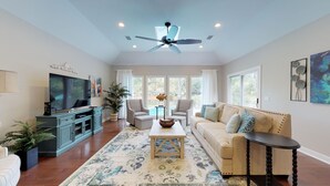 A spacious living room with a ceiling fan, a television, a sofa, two armchairs, a coffee table, and a side table. - Beautiful home on the 11-mile lagoon system with a large private pool! (Hilton Head)