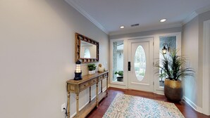 A hallway with a wooden console table, a mirror, a floor lamp, and a large potted plant. - Beautiful home on the 11-mile lagoon system with a large private pool! (Hilton Head)