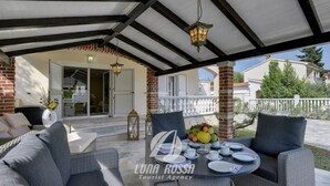 A covered outdoor seating area with wicker furniture, a table set for dining, and a fruit bowl. - Villa Sonja is located directly on the sea (Medulin)