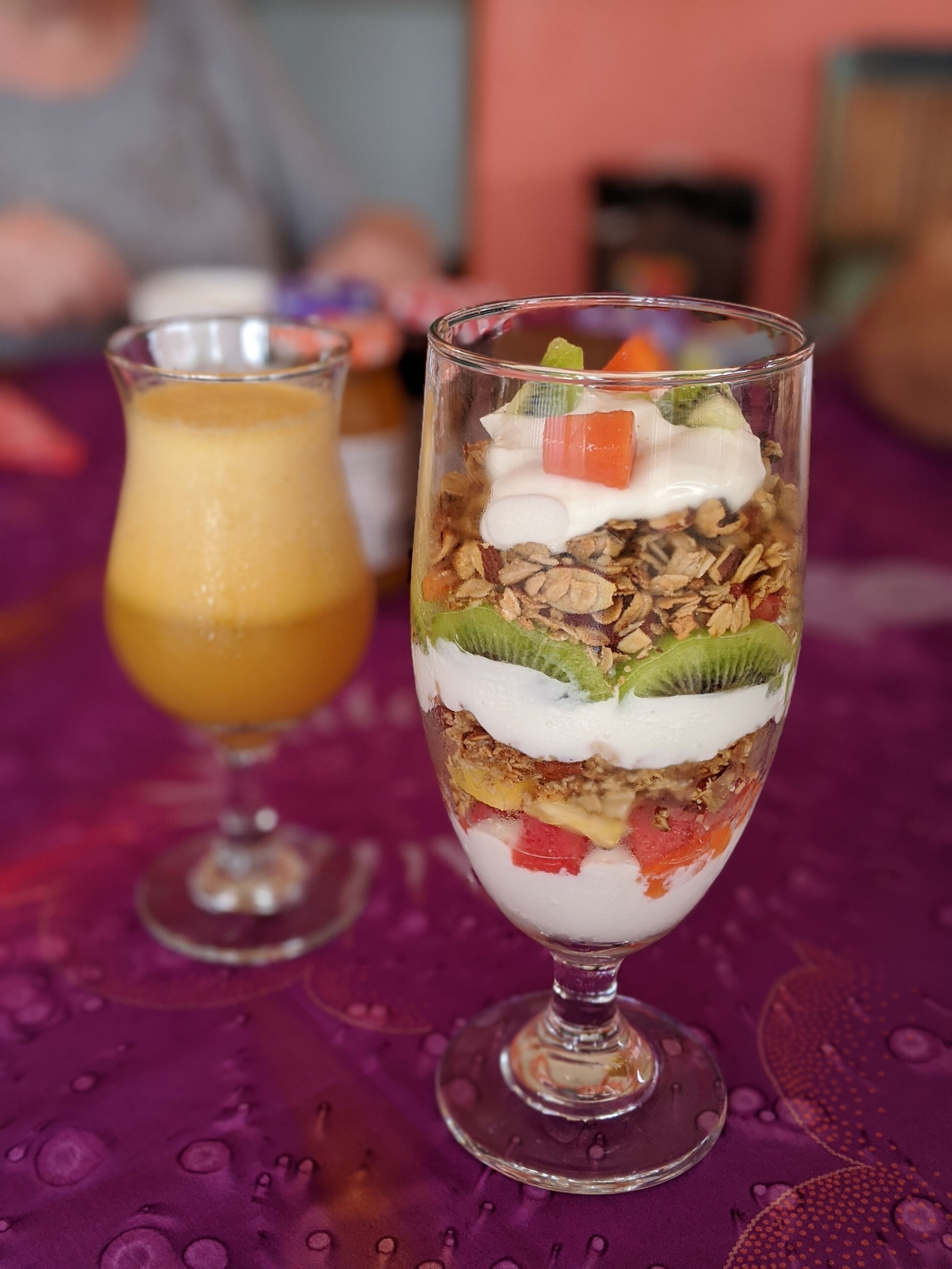 A layered dessert in a glass on a table with a purple tablecloth.