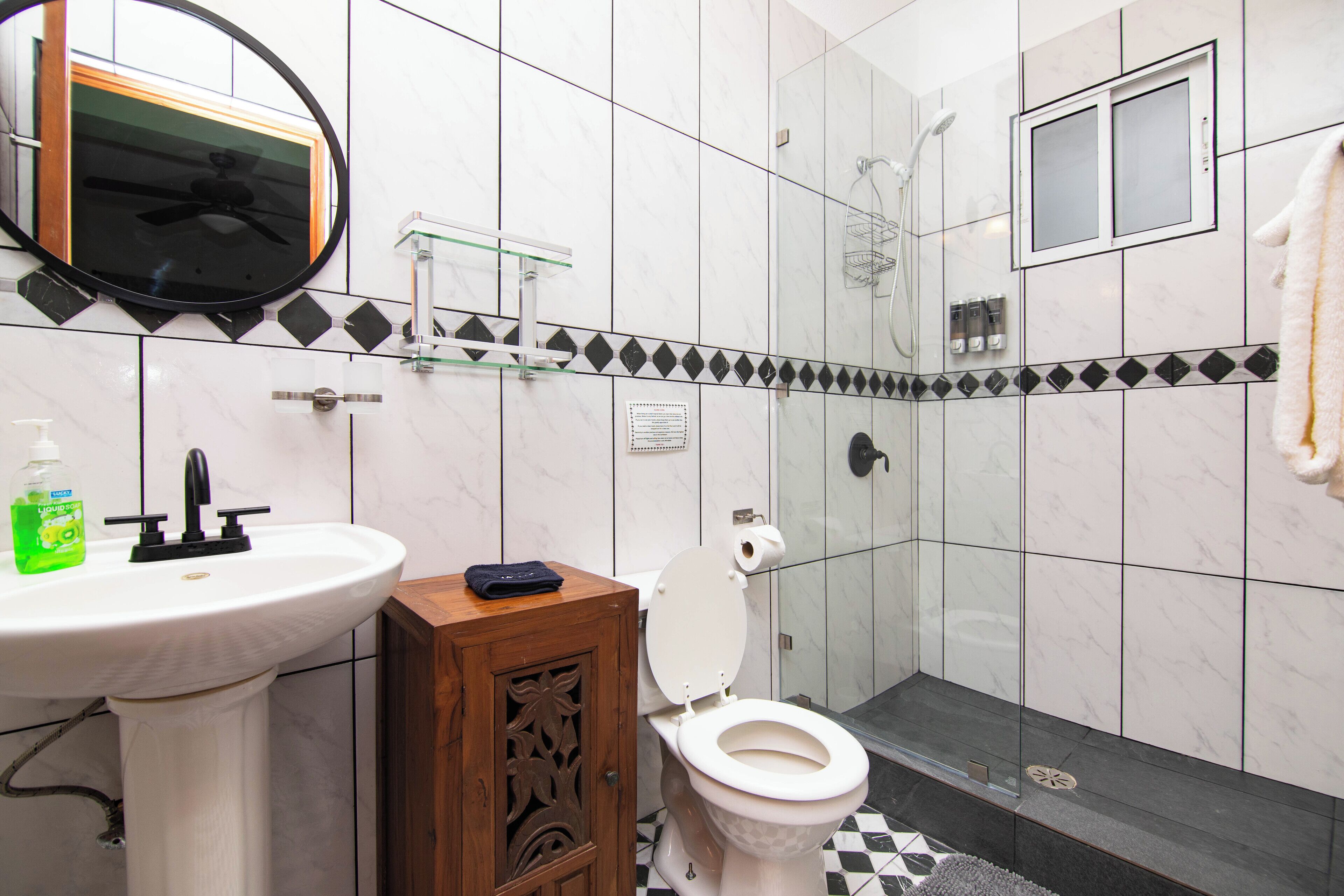 A bathroom with a white sink, a wooden cabinet, a toilet, a glass shower enclosure, and a towel hanging on the wall.