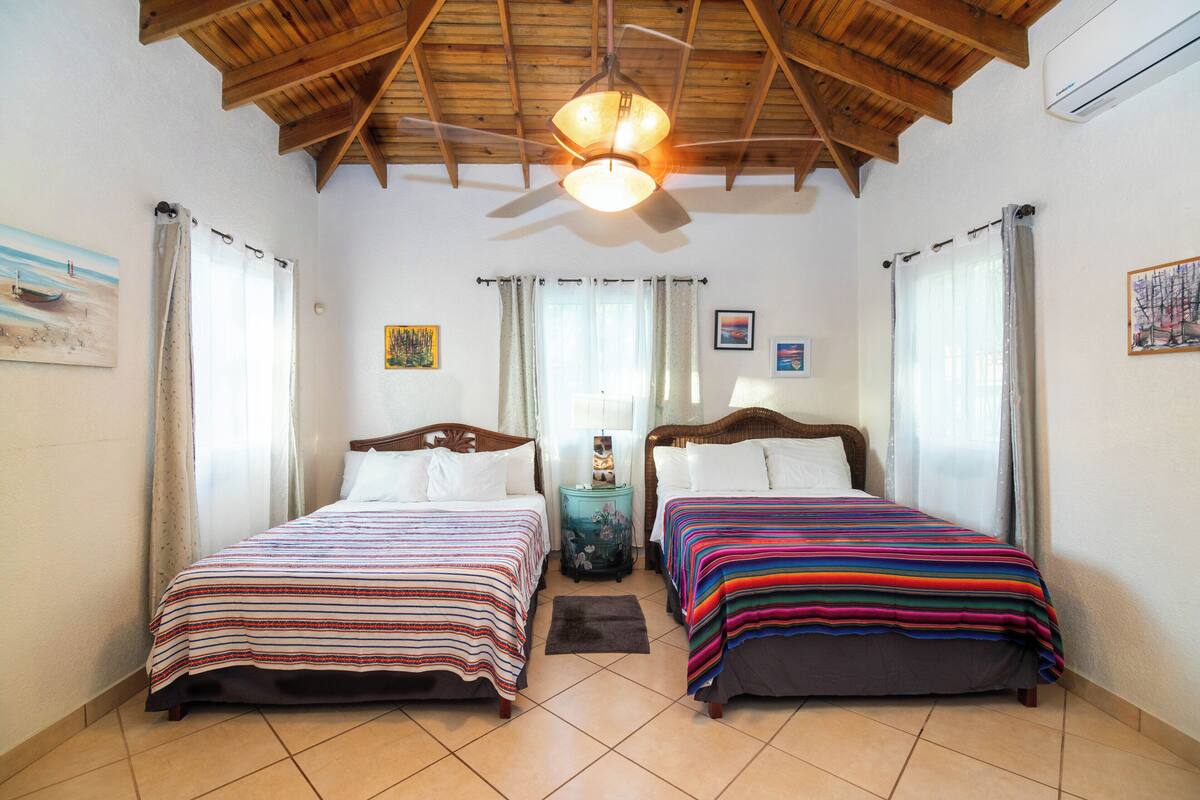 A room with two beds, a ceiling fan, and a small table with a lamp.