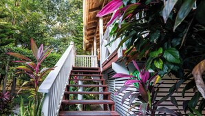 Eine Holztreppe mit weißen Geländern führt zu einer Veranda, umgeben von üppigem Grün.