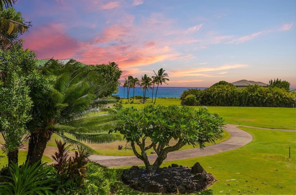 A golf course with a curved path, palm trees, and a view of the ocean at sunset.