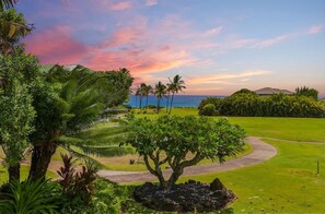 Un parcours de golf avec un tracé sinueux, des palmiers et une vue sur l’océan au coucher du soleil.