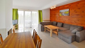 Una sala moderna con pared de madera, un sofá gris, una mesa de centro de madera y un comedor con mesa y sillas de madera.
