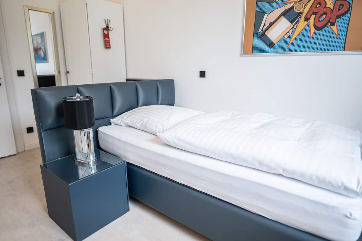 A modern bedroom with a bed, a bedside table, and a wall-mounted artwork.