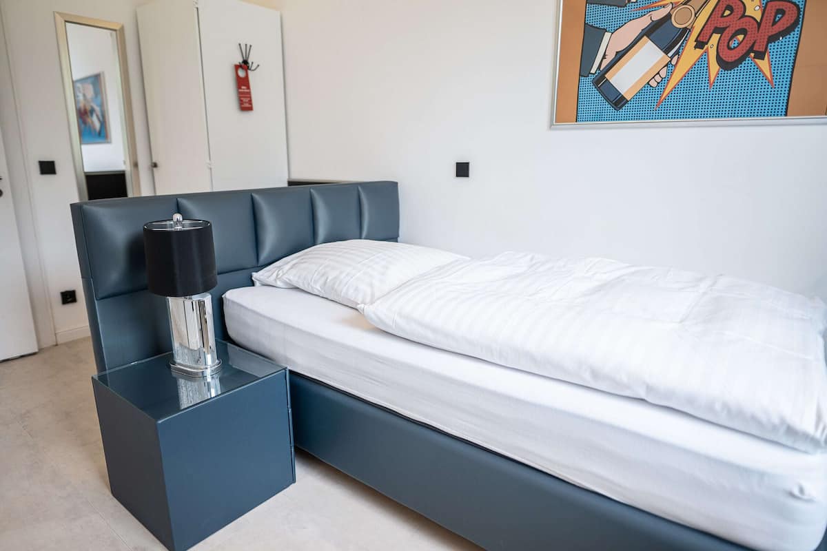 A modern bedroom with a bed, a bedside table with a lamp, and a wall art piece.