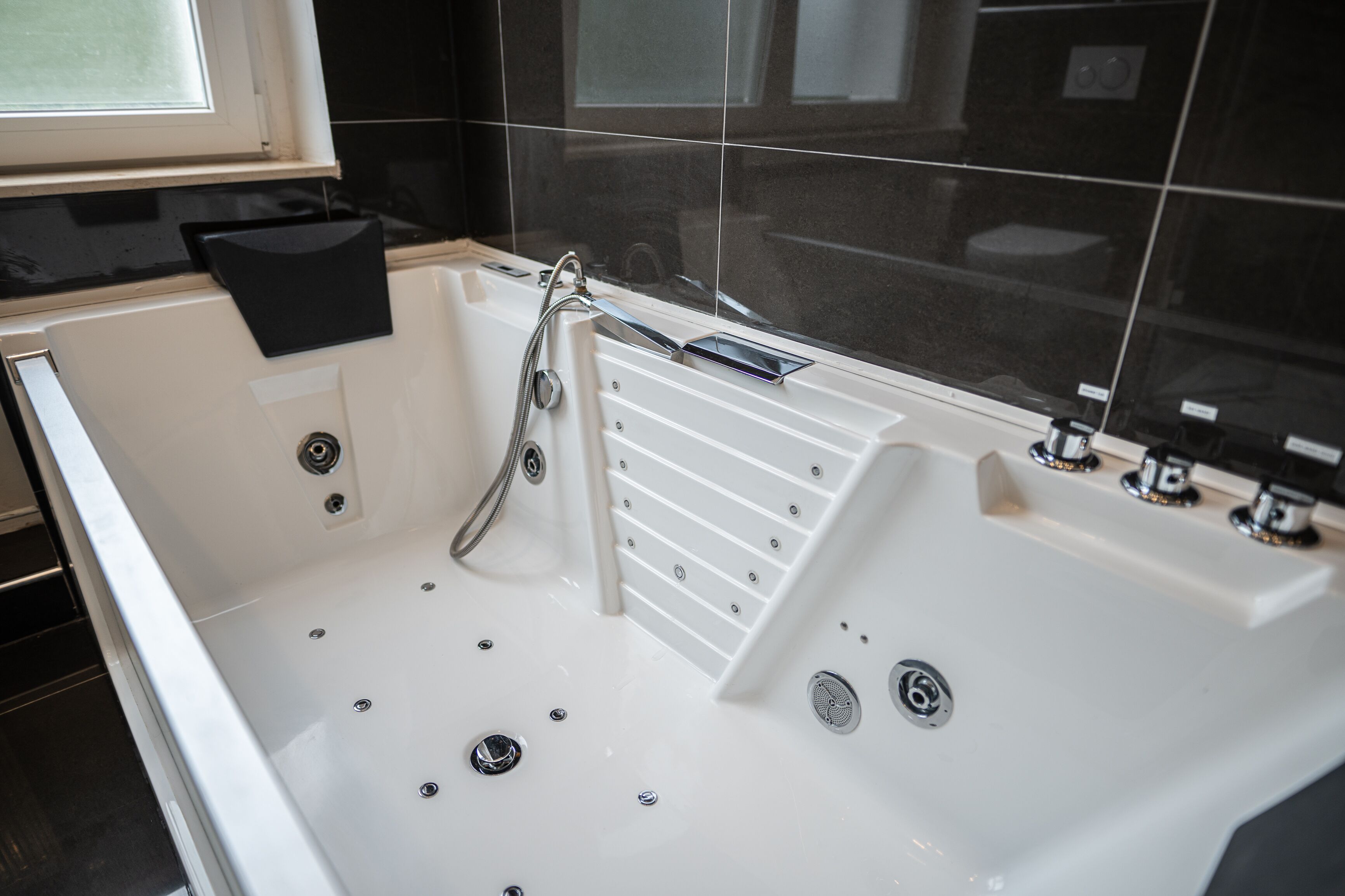 A modern bathroom with a large bathtub, a handheld showerhead, and a built-in seat.
