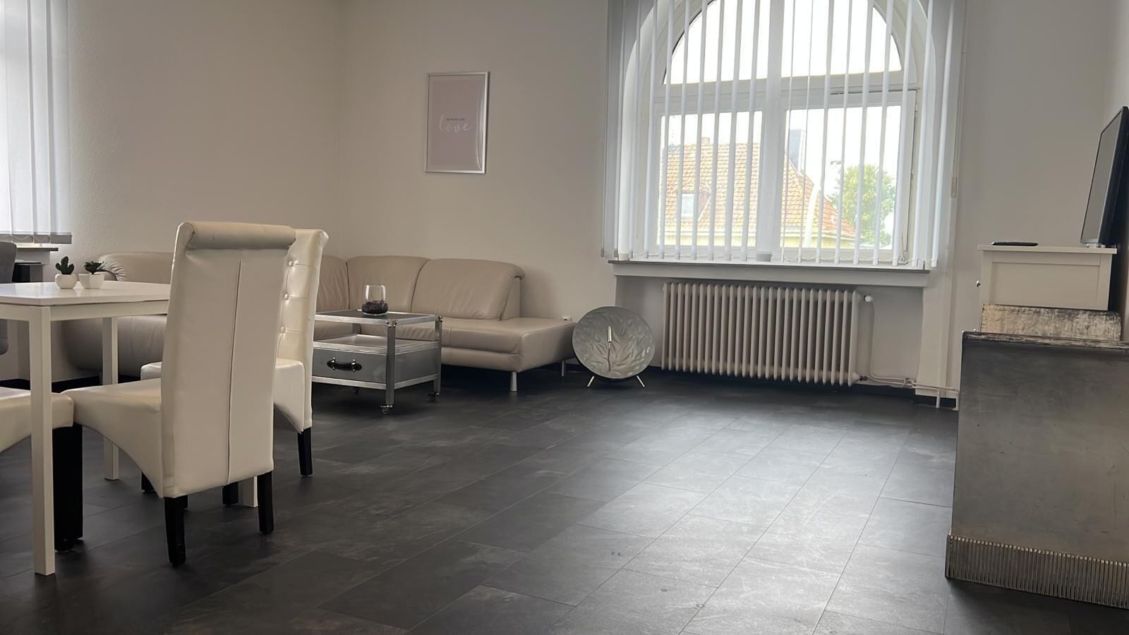 A modern living room with a dining area, a sofa, a coffee table, and a radiator.