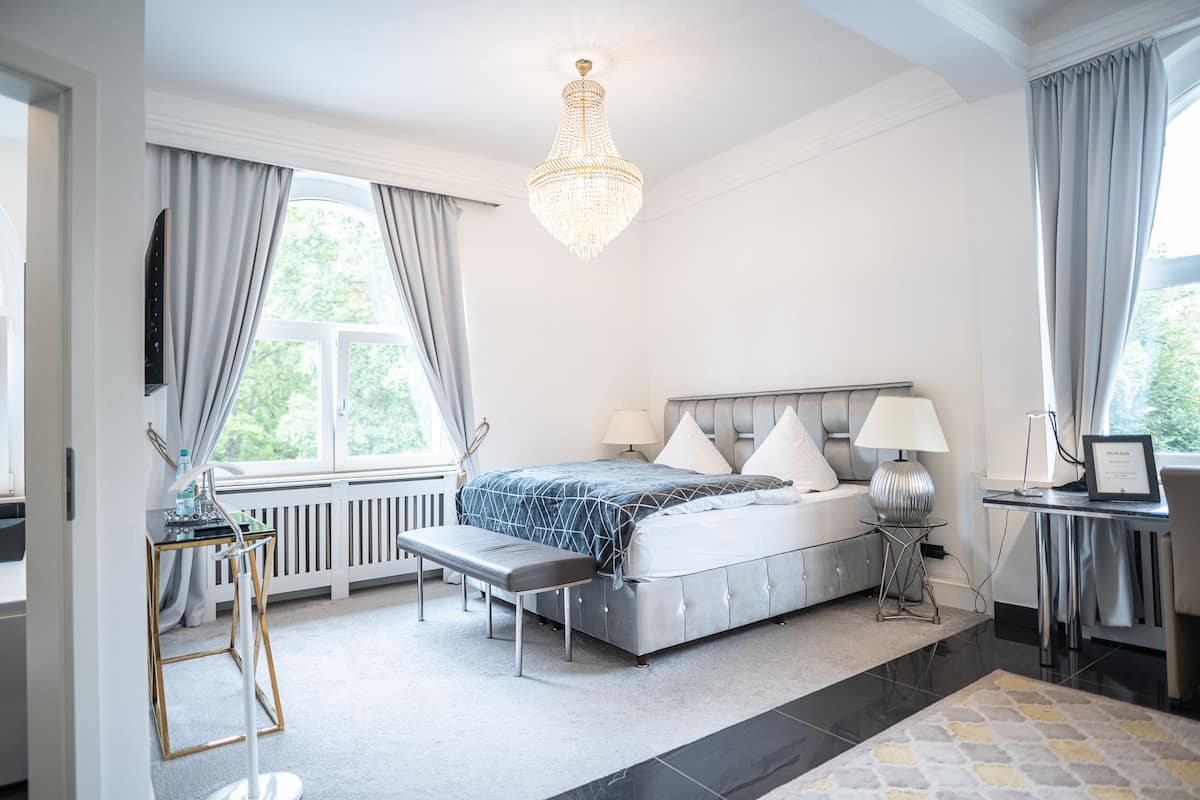 A modern bedroom with a large bed, bedside tables, a bench, a desk, and a chandelier.