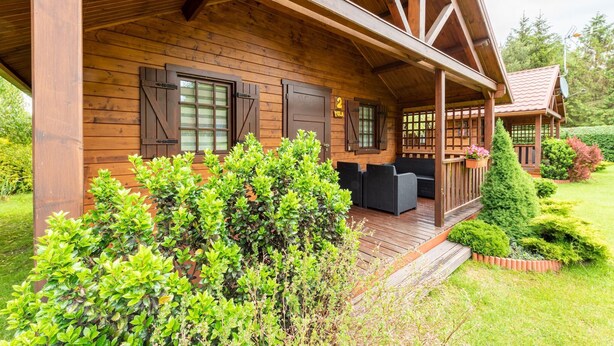 Eine Holzjagdhaus mit überdachter Veranda, einer kleinen Terrasse und einem gepflegten Garten.